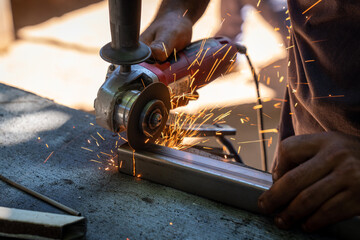 a man working cutting metal bar with a circular electric tool that shoots sparks