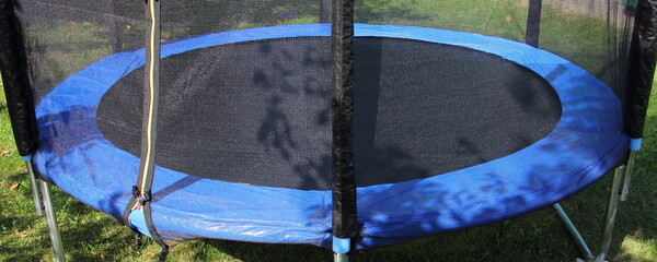 Empty 8ft trampoline with soft net fence on green grass background at Sunny summer day, outdoor sports