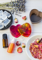 Making handmade soap with crystal clear melt and pour soap mixture. Ready to use pink and yellow tied soaps with rose petals and lavender blossoms in center surrounded by ingredients.