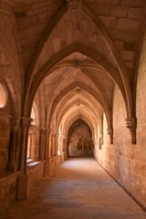 Fototapeta na wymiar View into a hallway of the Cistercian Gothic Claustro de los Caballeros cloister with its pointed arches in yellow pink sandstone at the Trappist Monasterio de Santa María de Huerta monastery, Spain