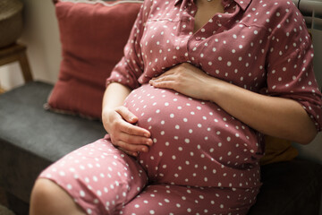 Pregnant woman sitting on couch and touch her belly.