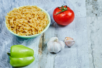 A bowl of raw pasta with tomato, pepper, and garlic on blue background