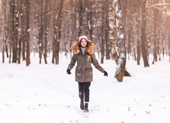 Young beautiful girl runs through the snow in the park in winter