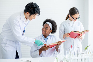 Asian teacher help and guide to African American young scientist child girl to analysis by read more data in the book in laboratory or classroom while other student also read textbooks.