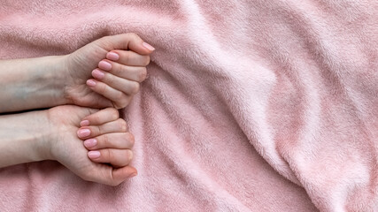 Female hands with beautiful manicure - pink nude nails on pale pink fluffy fabric, textile background with copy space