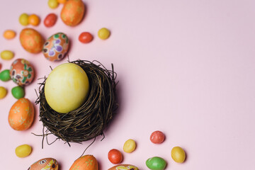 Painted yellow egg for the holiday of Easter in a nest of branches next to sweets and gingerbread cookies. Easter card on a pink background