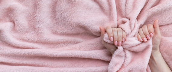 Female hands with beautiful manicure - pink nude nails on pale pink fluffy fabric, textile background with copy space. Wide banner