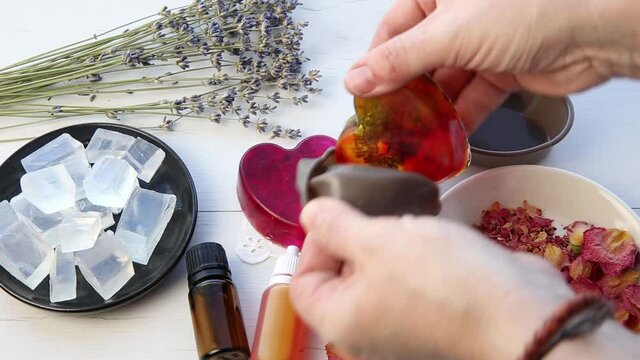 Making handmade soap with crystal clear melt and pour soap mixture. Ready to use pink and yellow tied soaps with rose petals and lavender blossoms in center surrounded by ingredients.