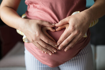 Pregnant woman with her daughter holding her belly and making a heart shape.