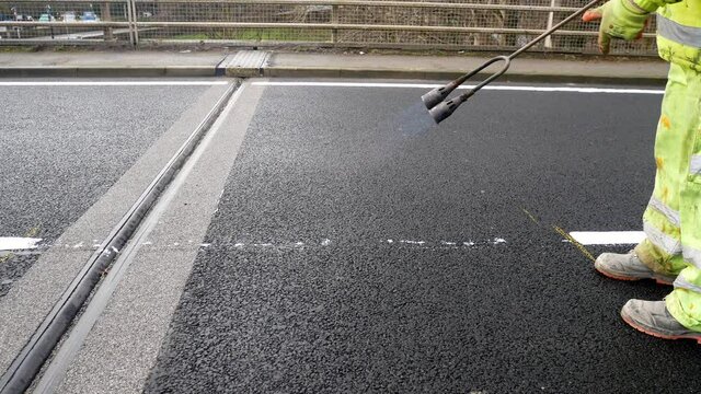 Council worker with propane gas flame torch melting tarmac road asphalt marking paint