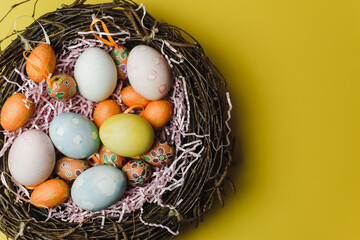 A nest of twigs and hay and a pink paper filler with pastel colored Easter eggs. Colored eggs for the holiday of light Easter. Easter card on a yellow background