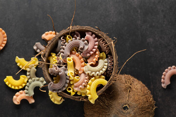 colored pasta in the form of handmade scallops in a coconut plate on a gray vintage background, top view