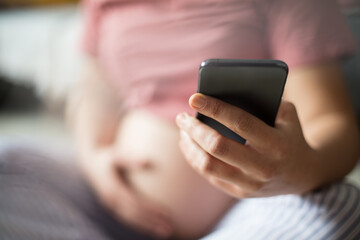 Pregnant woman sitting on floor at home and using mobile phone