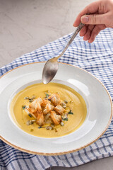 hand holding spoon above Autumn Butternut Squash Soup with Bread and seeds on the table