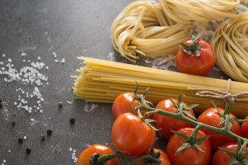 Raw pasta close up photo. Tagliatelle pasta and cherry tomatoes on a table. Healthy eating concept. 