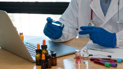 Fototapeta na wymiar COVID-19 Vaccine Trial Concept: A male doctor holds a syringe and a medicine bottle while preparing for injection. The doctor's hand held a close-up syringe on a table with a laptop.