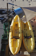 Two yellow plastic kayaks and paddles and stuff on a floating dock in an ocean boating harbor