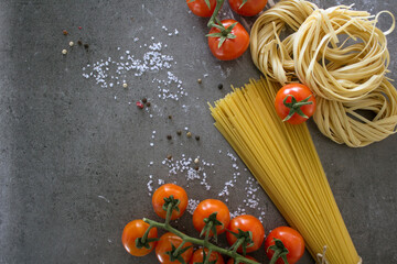 Raw pasta close up photo. Tagliatelle pasta and cherry tomatoes on a table. Healthy eating concept. 