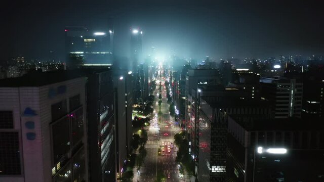 Beautiful aerial shot of Seoul Gangnam District at the night with CG light flare and volumetric fog. Camera moving between modern skyscrapers above the highway. 