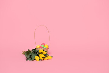 basket with colorful easter eggs and bouquet of yellow tulips on pink background