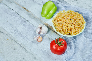 A bowl of raw pasta with tomato, pepper, and garlic on blue background