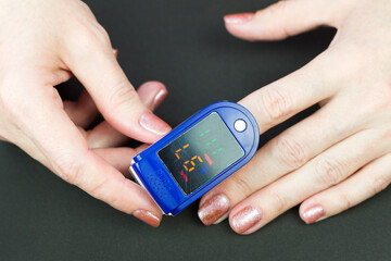 Oximeter on the finger of a female hand black background.