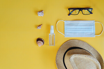 Travel under Covid-19 and new normal concepts. Top view of medical face mask, hand gel sanitizer, glasses and beach hat on yellow background. Creative ideas of prevent coronavirus.