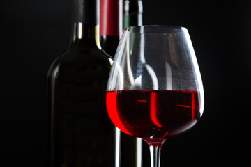 several different bottles of wine and a glass with red wine on a dark glossy background.