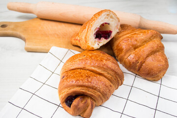 Rustic style. Tasty croissants and piece lay on linen fabric near wooden rolling pin on white table.