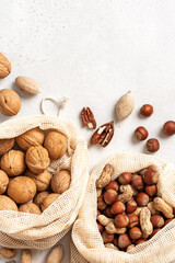 Walnuts, peanuts, hazelnuts, and pecans in shopping bags on a white background top view. Copy space for text. Various nuts.