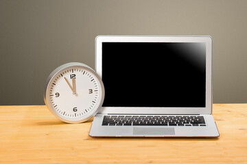 mocap Laptop and clock with arrows at five to twelve on a wooden table.