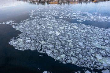 Background of cracked pieces of ice shards on the water. Ice floes floating on the river in the dark water in mosaic form. Winter contrast black and white backdrop. 