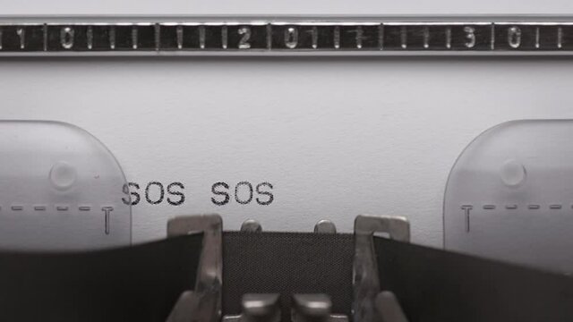 Typing text SOS on vintage manual typewriter. Close up of writes word on white paper. Shot in macro 4K resolution. Typing a Morse code distress signal - The phrase save our souls.