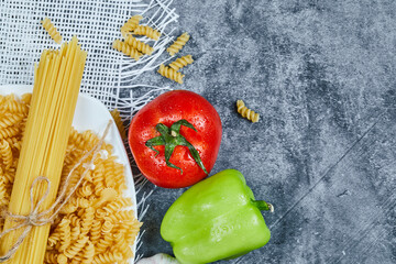 A bowl of raw pasta with tomato, pepper, and garlic on blue background