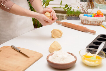the process of rolling out the dough at home on the table is the hands of a woman for making cruffins festive pastries for Easter . side view of a bright kitchen , with painted eggs