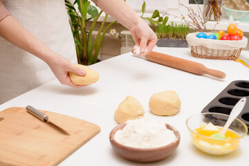 the process of rolling out the dough at home on the table is the hands of a woman for making cruffins festive pastries for Easter . side view of a bright kitchen , with painted eggs