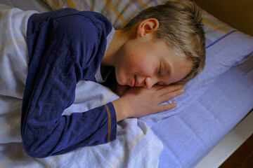 cute blonde boy in blue pajama sleeping and smiling in dream in bed close-up. Kids bedroom....