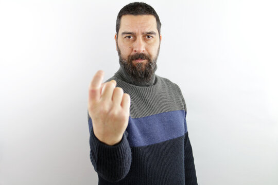 Man with beard wearing winter sweater and glasses beckoning come here gesture with hand inviting 