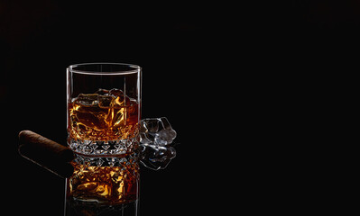 Whiskey with ice or brandy in glass with cigar on black background. Whisky with ice in glass. Whiskey or brandy. Selective focus. - obrazy, fototapety, plakaty