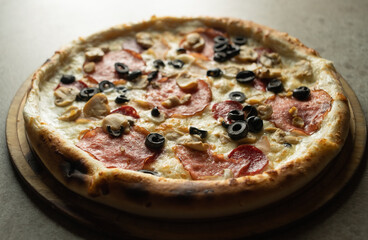 Delicious Italian pizza with sausage and mozzarella close-up on a gray background. Ready-made pastries in a pizzeria.