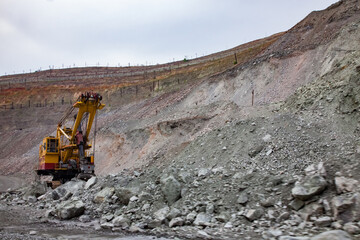 Open-pit mining iron ore in quarry. Excavator loads rocks in Caterpillar quarry truck.