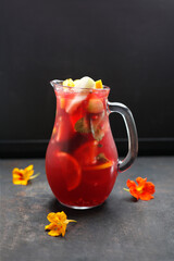 A jug of a colourful lemonade, drink, red sangria with fresh fruits, on a black stony background.