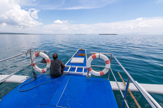 A Filipino boatman rests near the bow of a tourist bangka or outrigger cruising through calm glassy waters in Bohol, Philippines.