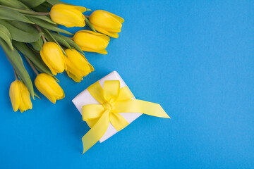 Top view of gift box and yellow tulips on the blue background