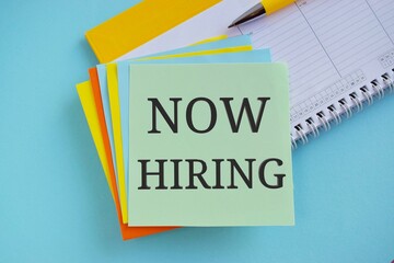 Now hiring written on colorful sticky note. light blue background