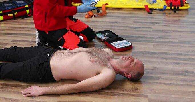 Reanimation of patient with defibrillator. Male paramedic in red scrubs teaching students correct procedure on using defibrillator machine. Application Defibrillator on CPR training