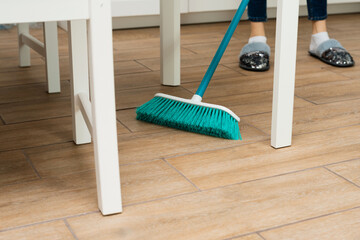 people, housework, cleaning and housekeeping concept - close up of woman legs with broom sweeping floor at home