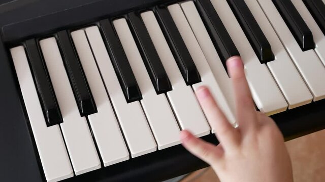 Close-up of the hand of a little boy pushing the white keys of a synthesizer one by one learning to play it