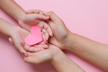 Adult and child hands holding red heart over pink background. Love, healthcare, family, insurance, donation concept