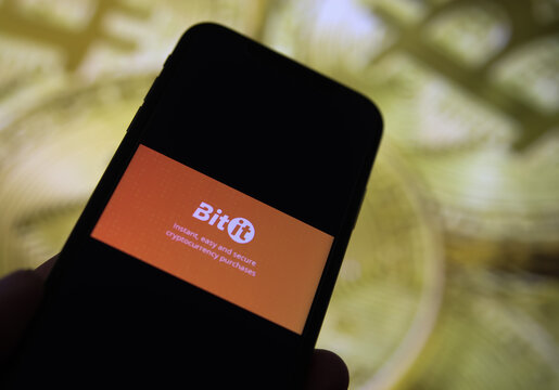 Viersen, Germany - February 9. 2021: Closeup of mobile phone screen with logo of bitit lettering trading platform, blurred bitcoins background
